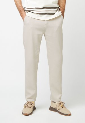 Beige geweven broek met een rechte pasvorm, voorzien van zakken en een gladde textuur, gecombineerd met lichtbeige gebreide sneakers.