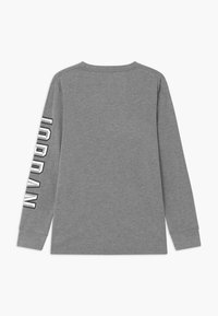 Langärmliges graues T-Shirt aus Baumwolle. Mit Rundhalsausschnitt und großem, vertikal auf dem linken Ärmel aufgedrucktem "JORDAN"-Text in Weiß.