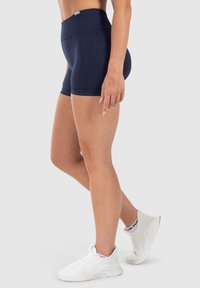 Marineblauwe hoge sportshorts gemaakt van rekbaar materiaal, met een gladde textuur en een aansluitend ontwerp. Draagt witte lichtgewicht sneakers.