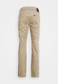 Béžové kordurové kalhoty s rovnými nohavicemi, které mají dvě zadní kapsy a tmavě hnědý kožený detail na pásu.