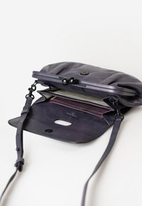 Borsa a tracolla in pelle viola con chiusura a patta, dotata di un interno a righe, tracolla regolabile e dettagli in metallo nero.