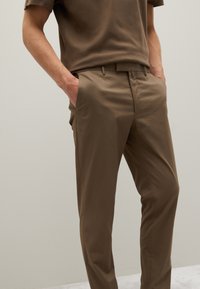 Bruine op maat gemaakte broek met een gladde textuur, slim fit, zijzakken en een nette tailleband. Gepromoot met een bijpassend bruin T-shirt met korte mouwen.