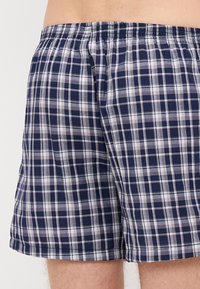 As boxers de homem em azul e branco em padrão xadrez apresentam uma cintura elástica e um tecido leve e respirável. O design inclui um padrão xadrez clássico.