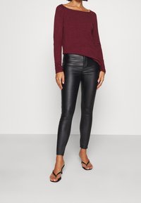 Maglietta a maniche lunghe bordeaux abbinata a leggings neri in ecopelle e ciabatte nere. La maglietta ha un scollatura a barca e una vestibilità comoda.