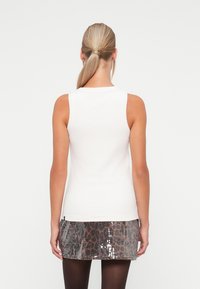 Valge soonikkoes tank top, mis on kombineeritud sädelevate halli ja pruuni loomapritsi seelikutega, esitades sale istuvuse ja tekstuuritud kangast.