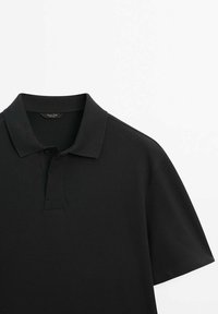 Polo noir à manches courtes avec col et patte à deux boutons, posé à plat sur fond blanc, montrant la partie avant supérieure.
