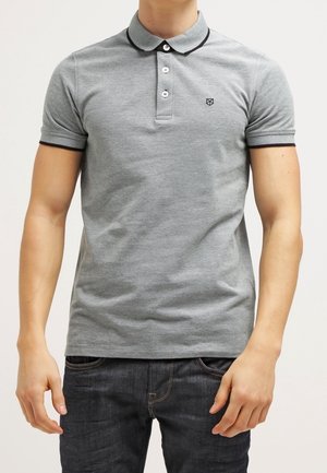 Person iført en tætsiddende grå polo med sort kant på krave og ærmer, kombineret med mørkeblå jeans.