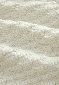 Textured white knitted fabric featuring a diamond pattern, with raised stitches providing a soft, thick appearance.