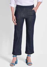 Pantalons en denim bleu foncé à coupe ample, avec une taille plate, des poches latérales et des ourlets raccourcis, associés à des sandales à talons bleues.