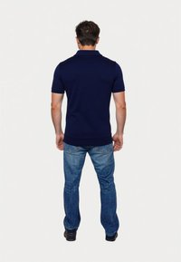 Camisa polo de manga corta azul marino con cuello clásico, combinada con jeans azul claro, vista desde la parte trasera, mostrando un diseño ajustado.