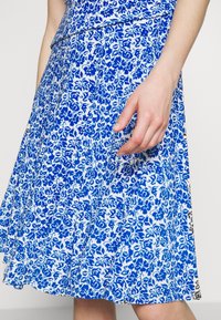 Niebieska i biała spódnica w kwiatowy wzór, rozkloszowany krój, lekki materiał, midi długość, o gładkiej fakturze i dopasowanej talii.