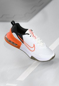 Baskets Nike Air Max blanches et orange avec une tige en mesh et une semelle à coussin d'air visible, présentées sur un fond gris.