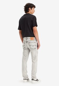 Black short-sleeve t-shirt paired with light gray distressed denim jeans. Notable label on the back of the jeans. White sneakers with black accents.