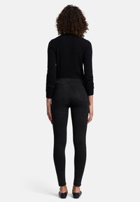 Jeans skinny noirs en denim, avec une taille mi-haute, poches arrière, et un design épuré et ajusté. Portés avec des chaussures plates.