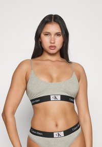 Sivé bavlnené bralette s tenkými ramienkami a čiernym elastickým pásom s logom "Calvin Klein". Kompletované s ladícími sivými nohavičkami.