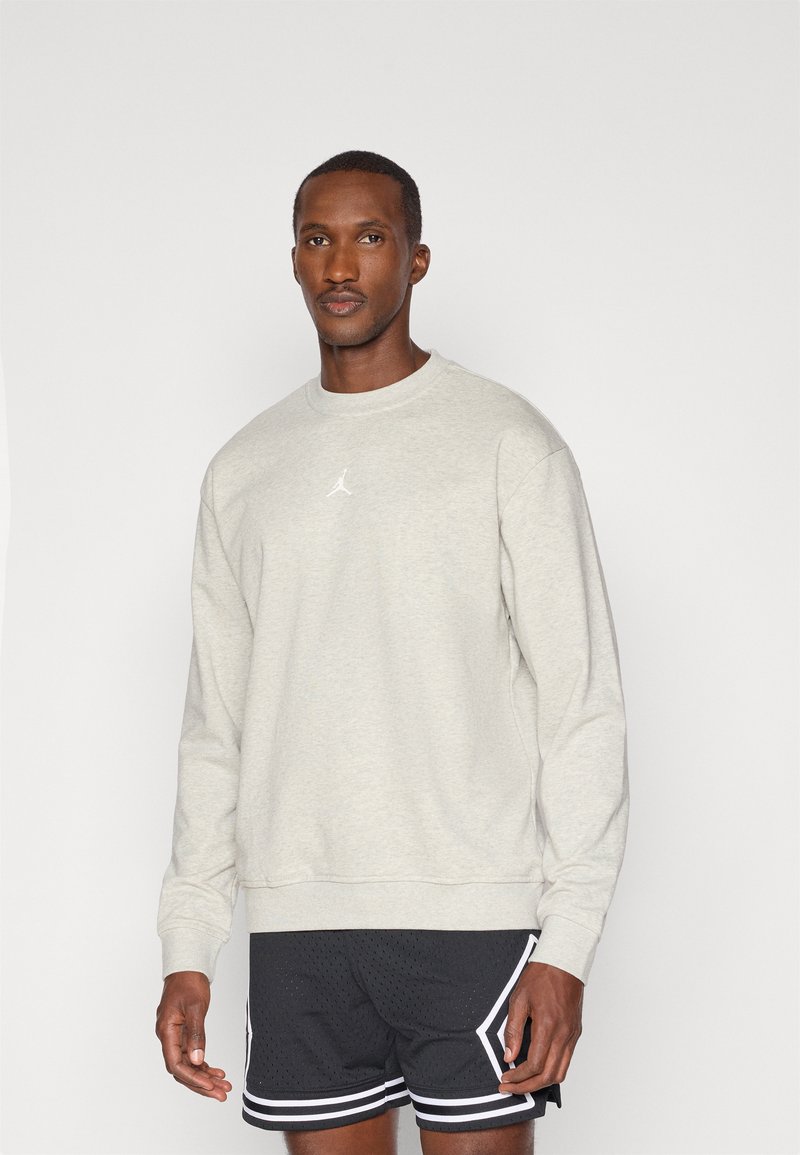 Sudadera gris claro de tejido suave, con cuello redondo y un pequeño logo blanco en el pecho, combinada con pantalones cortos deportivos negros.