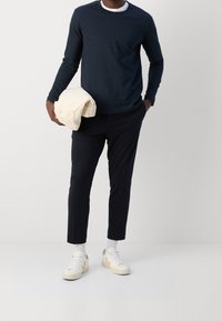 Granatowa koszula z długim rękawem, kremowy uchwyt w ręku. Slim fit czarne spodnie, białe tenisówki z kremowymi akcentami. Minimalistyczny design, gładkie materiały.