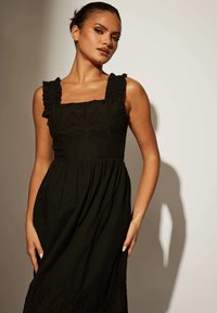 Svart klänning med volangband, fyrkantig halsringning och broderade detaljer. Utställd kjol och lätt material.