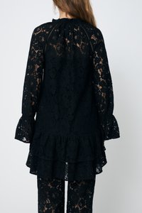 Tunică din dantelă neagră, cu mâneci lungi, hem ruffled, model floral și decolteu plisat, purtată peste pantaloni din dantelă asortați.