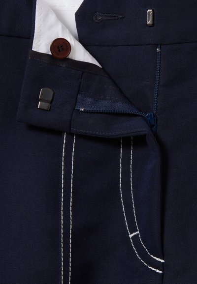 Pantaloni blu scuro con zip, bottone marrone e cuciture bianche a contrasto su tasche e cuciture. Tessuto morbido.