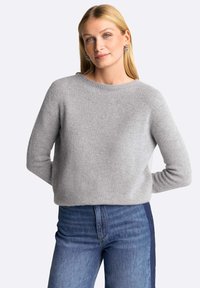 Pulover gri din tricot, cu guler rotund, mâneci lungi și o textură moale, asortat cu blugi albaștri cu o ușoară decolorare.
