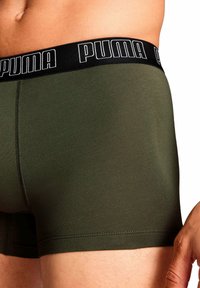 Boxers ajustados de algodón verde con un cinturón elástico negro que presenta el logo de "PUMA" en blanco, mostrando una textura de tela suave y un diseño que se ajusta bien.