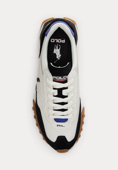 Weiße und schwarze Polo Ralph Lauren Sneaker mit brauner Sohle, weißen Schnürsenkeln, blauem Zungen-Detail und Polo-Logo innen sowie auf der Zunge.