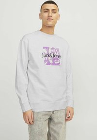 Grå sweatshirt med rund hals, med et lilla grafisk design og sort tekst "Jack & Jones EST. 1990." Tekstureret stof med lange ærmer.