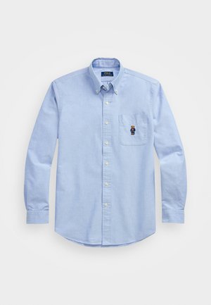 Jasnoniebieska koszula z długim rękawem, z kołnierzykiem i kieszonką na lewym piersiu, zdobiona małym haftowanym wzorem niedźwiedzia.