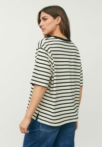 Stribet t-shirt i creme og sort, med korte ærmer, en rund halsudskæring og sidedelinger i kanten for let bevægelse.
