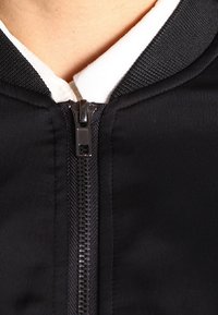Close-up of a black jacket zipper partially zipped over a white collared shirt on a person’s neck and upper chest.