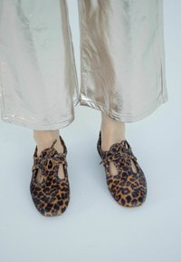 Scarpe con stampa leopardata, design con ritagli e dettagli con lacci, abbinate a pantaloni larghi argentati lucidi. Contrasto tra tessuti testurizzati e motivi.