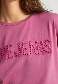 Rosa bomulls t-shirt med "PE JEANS" broderat i mörkare rosa med hål detaljer, rundad halsringning och korta ärmar.