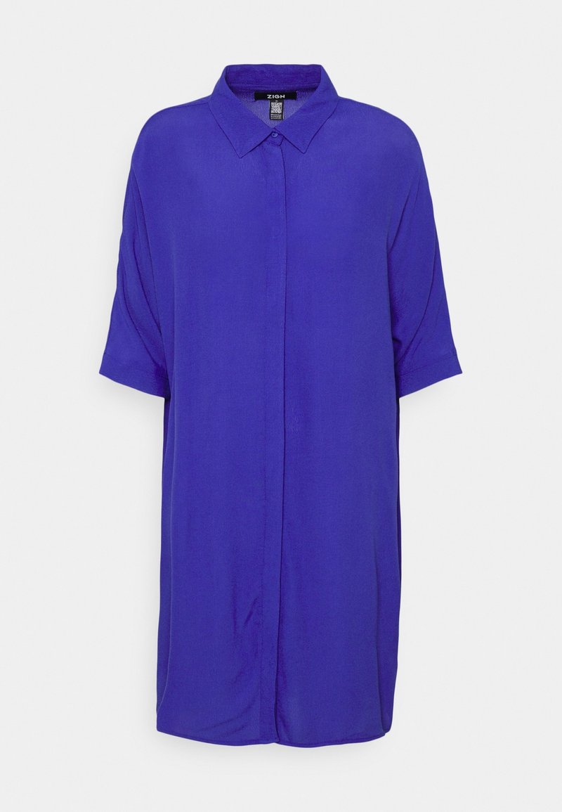 Robe-chemise violette ample, à manches courtes, longueur au genou, avec un col pointu et des boutons avant cachés sur un fond uni.