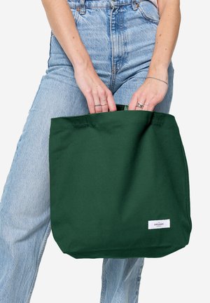 Zielona bawełniana torba na ramię z dwoma uchwytami, prostokątny kształt, gładka tekstura i mała biała metka z napisem "ORGANIC" z przodu.