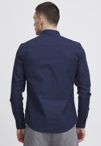 Camisa de manga larga azul marino hecha de una tela suave, con una cintura ajustada, puños abotonados y un cuello crujiente, que presenta un diseño minimalista.