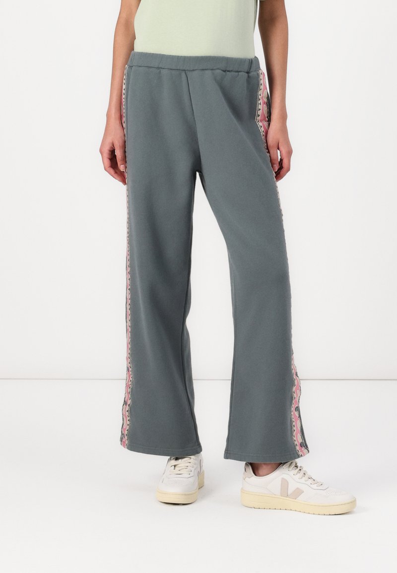 Grå vide ben sweats med blødt stof, med en blomster mønstret lyserød stribe langs siden, parret med hvide sneakers.