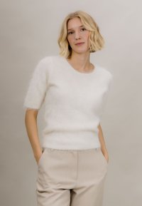 Hvit fluffy genser med korte ermer, myk tekstur, rund hals, kombinert med lyse beige bukser med høyt liv. Enkel og ren design.