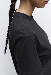 T-shirt nera in cotone con collo tondo. Il tessuto appare liscio con maniche corte, enfatizzato da dettagli di cucitura discreti.