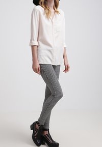 Blusa rosa chiaro con tasca, maniche a tre quarti, abbinata a leggings a quadri bianchi e neri. Scarpe con tacco nere e con cinturini.