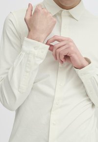 White long-sleeve shirt made of soft fabric, featuring a collar, button closure, and neatly folded cuffs with tab detail.