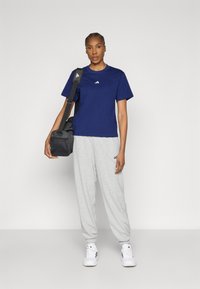 Tengerészkék rövid ujjú pamut póló kis fehér logóval, szürke melegítőnadrággal és fehér sportcipővel párosítva. Fekete válltáska.