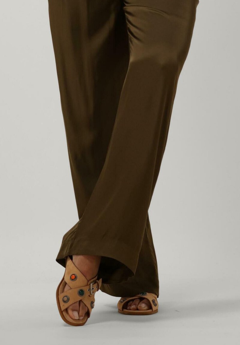 Bruine wijde broek met tan sandalen met decoratieve gekleurde studs en een gesp, waarbij de tenen en de structuur van de voet zichtbaar zijn.