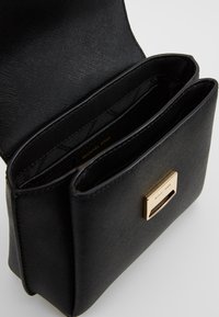 Zwarte leren handtas met een gestructureerd oppervlak, voorzien van een sluiting met goudkleurige hardware en drie binnenvakken.