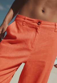 Leuchtend orangefarbene Leinenhose mit glatter Textur, ausgestattet mit einem einzelnen Knopf in der Taille und seitlichen Taschen. Maßgeschneiderte Passform und gerade Beinform.