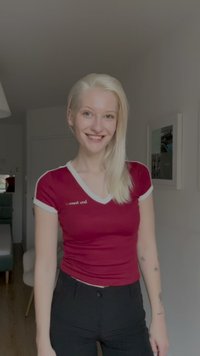 Red fitted T-shirt with white trim, featuring text on the chest; paired with black trousers. Smooth fabric, short sleeves.