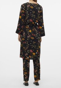 Blommigt svart plagg med en lång jacka med vida ärmar och matchande figurnära byxor. Materialet verkar slätt; detaljer inkluderar olika färgglada blommor.