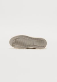 Lichtgrijze sneakerzool met een gestructureerd, ribbelpatroon. Ronde vorm met een gladde rand en een klein rechthoekig detail nabij het midden.