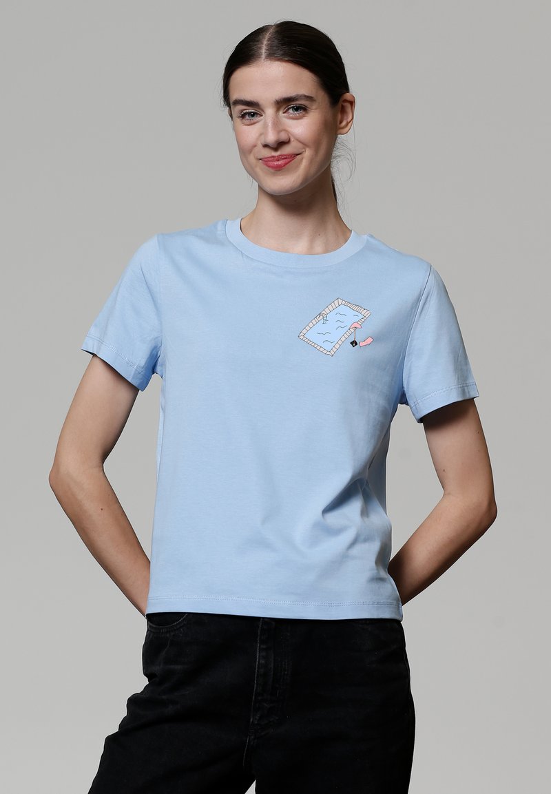 T-shirt en coton bleu clair avec un col rond, des manches courtes et un graphisme de piscine et de bouée rose en cartoon sur le devant.