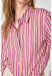 Camicia button-up a righe con linee verticali in rosa, viola e giallo, dotata di colletto e bottoni simili a perle. Tessuto morbido.